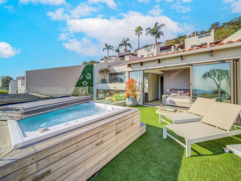 A modern outdoor terrace featuring a built-in hot tub, artificial turf, and seamless indoor-outdoor flow through large sliding glass doors.