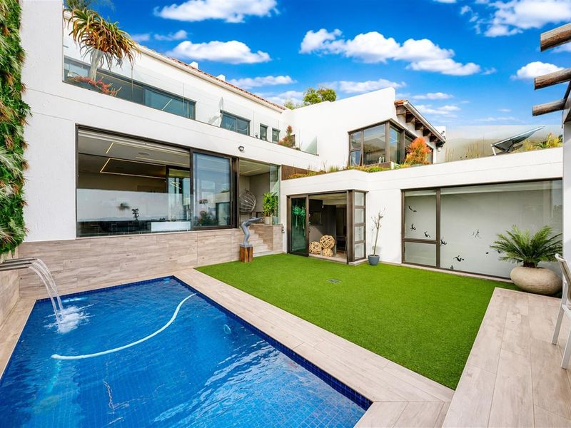A modern outdoor pool area featuring a tiled swimming pool with a water feature, artificial lawn, and seamless access to the home via sliding doors.
