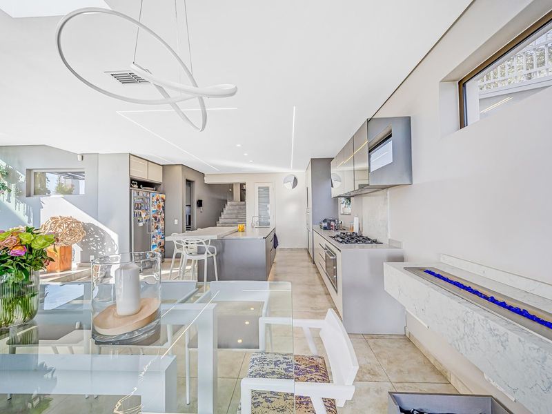 Modern open-plan living area featuring a sleek kitchen with stone countertops, integrated appliances, linear lighting, and a contemporary fireplace.