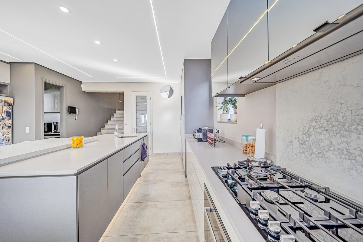 Modern kitchen featuring a large island, stone countertops, gas hob, integrated appliances, and sleek cabinetry with contemporary recessed lighting.