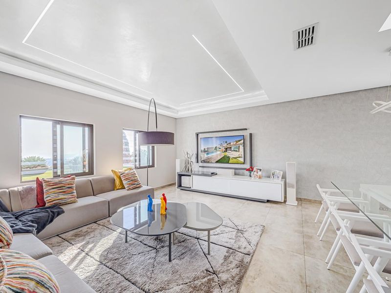 A modern open-plan living and dining area featuring a tray ceiling with recessed lighting, tiled floors, and a sleek built-in media console.