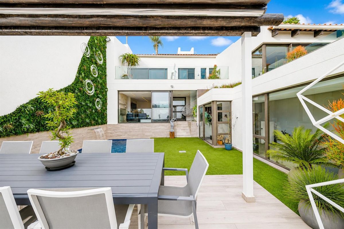 A modern rear courtyard featuring a swimming pool, artificial lawn, vertical garden, and seamless indoor-outdoor flow through large sliding glass doors.