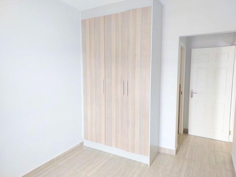 A bright, empty bedroom featuring modern light wood-finish built-in wardrobes and neutral tiled flooring.