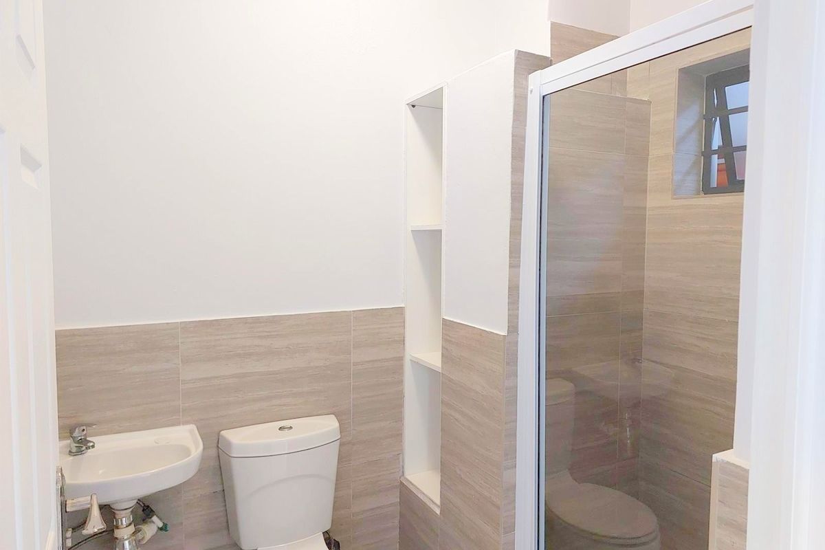 A clean, modern bathroom featuring a wall-mounted basin, toilet, and a glass-enclosed shower with neutral-toned wall tiles and built-in shelving.