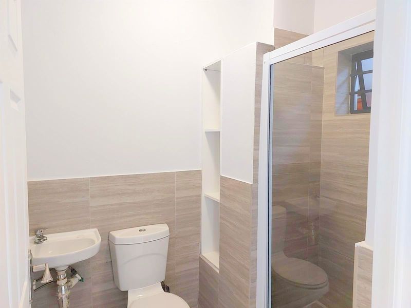 A clean, modern bathroom featuring a wall-mounted basin, toilet, and a glass-enclosed shower with neutral-toned wall tiles and built-in shelving.