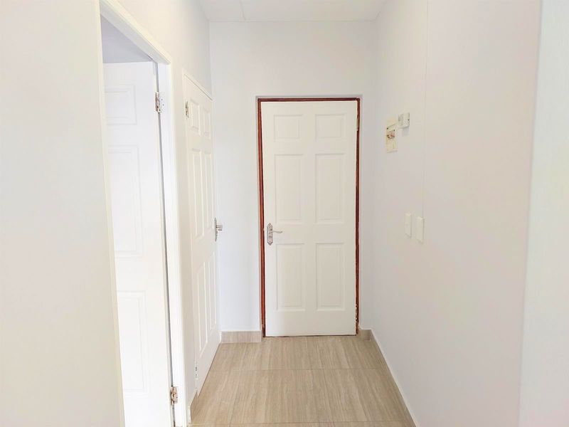 A clean, bright hallway featuring neutral tiled flooring and white panel doors, providing a simple and well-maintained transition space within the apartment.