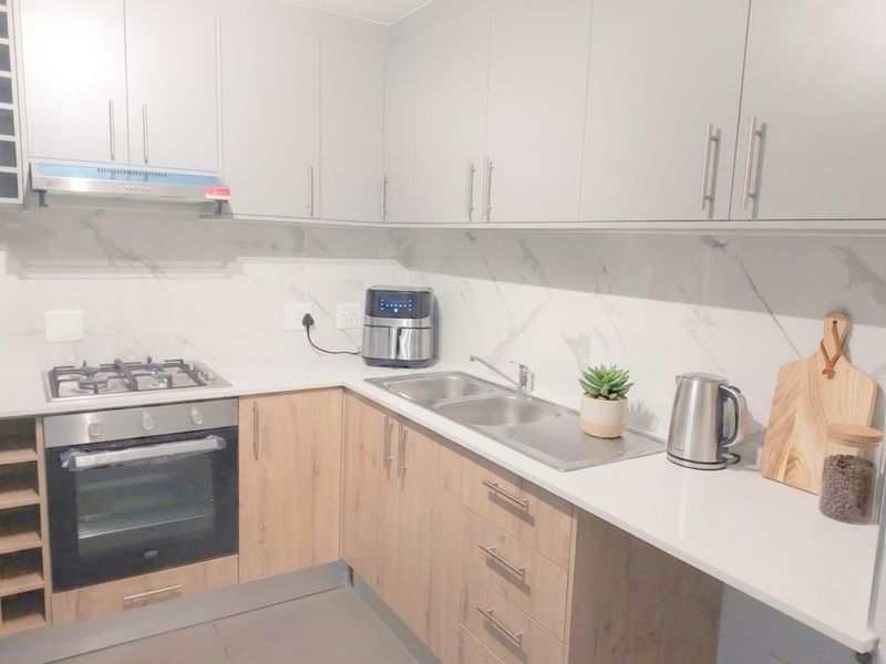 Modern kitchen featuring light wood-tone lower cabinetry, sleek grey upper cabinets, marble-look splashback, and integrated stainless steel appliances.