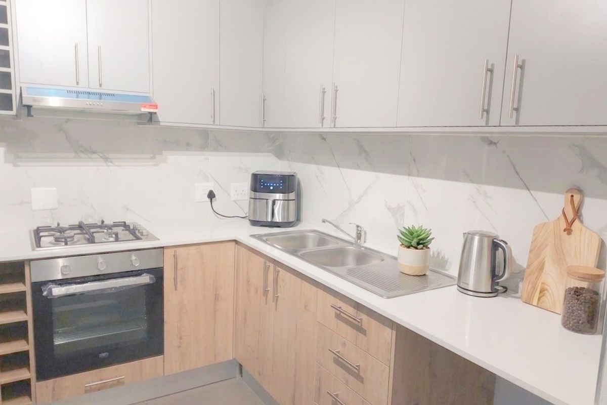 Modern kitchen featuring light wood-tone lower cabinetry, sleek grey upper cabinets, marble-look splashback, and integrated stainless steel appliances.