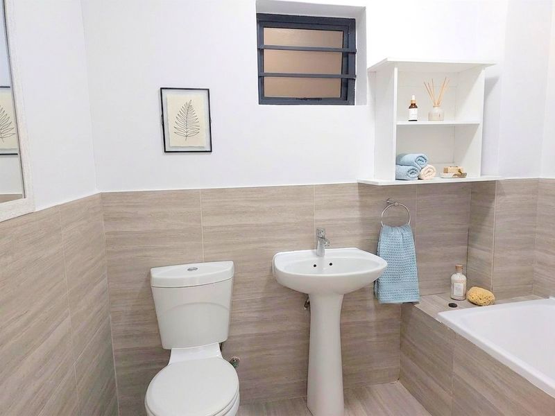 A clean and well-maintained bathroom featuring a pedestal basin, toilet, and bathtub with neutral-toned wall and floor tiling.