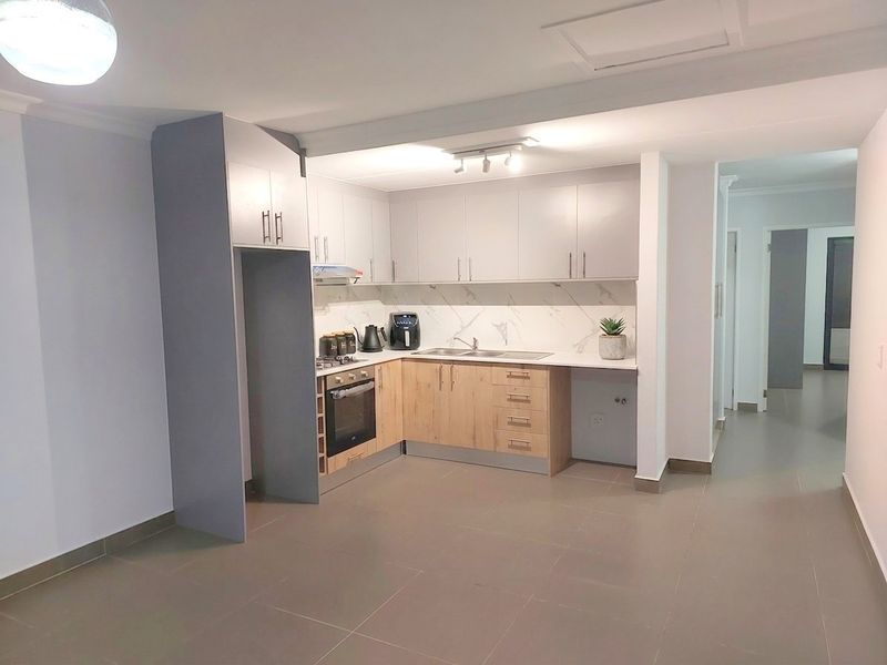 Modern kitchen featuring two-tone cabinetry, built-in oven and hob, marble-look backsplash, and neutral tiled flooring in an open-plan layout.