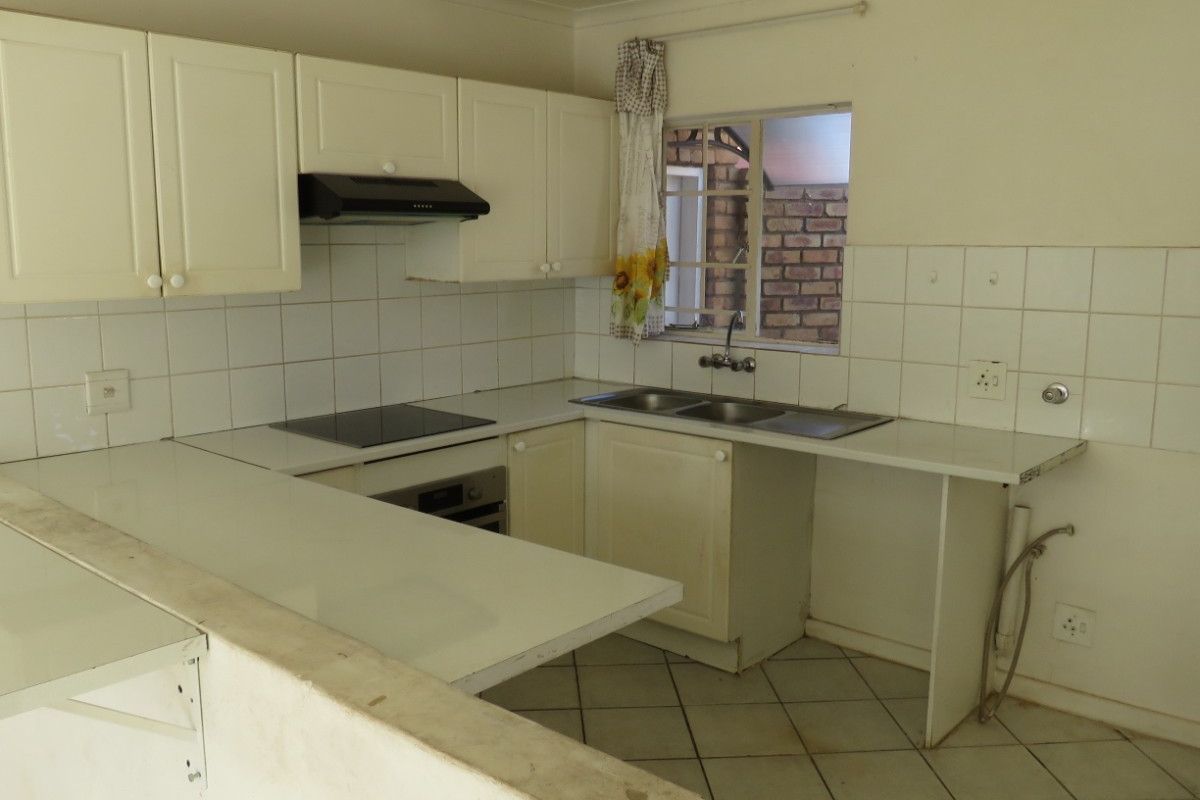 A dated kitchen featuring white cabinetry, laminate countertops, an electric hob, and tiled flooring, offering a blank canvas for renovation.