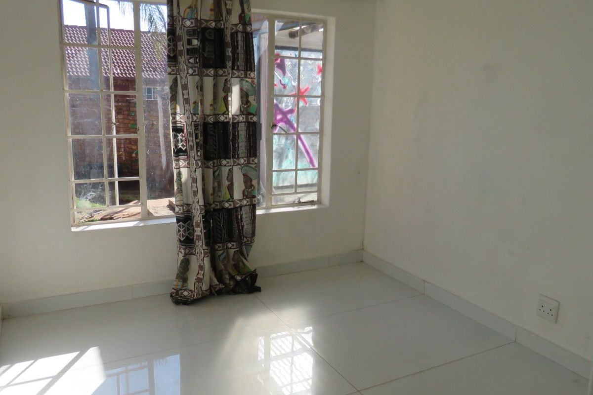An empty bedroom featuring white tiled flooring and a window with security bars, providing a blank canvas for potential interior design.
