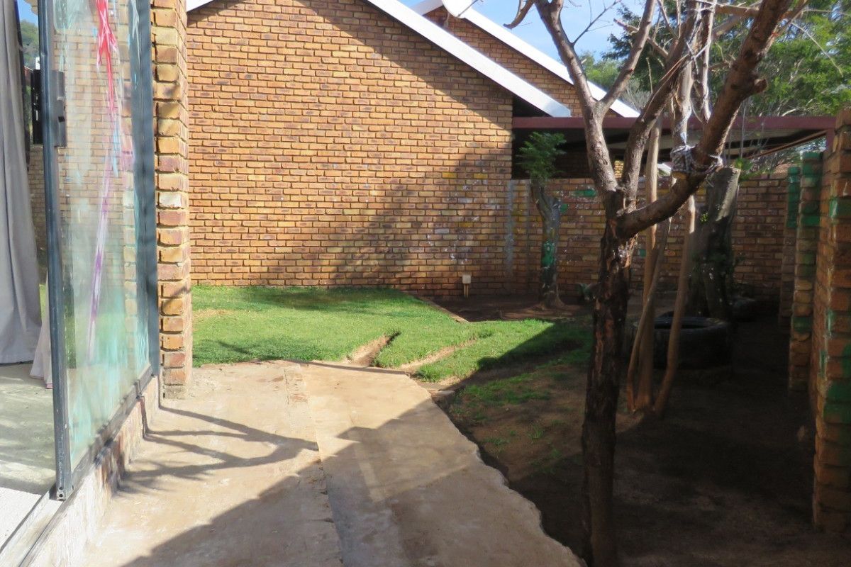 A rear exterior view showing a face brick house facade, a concrete pathway, and a small garden area with patchy lawn.