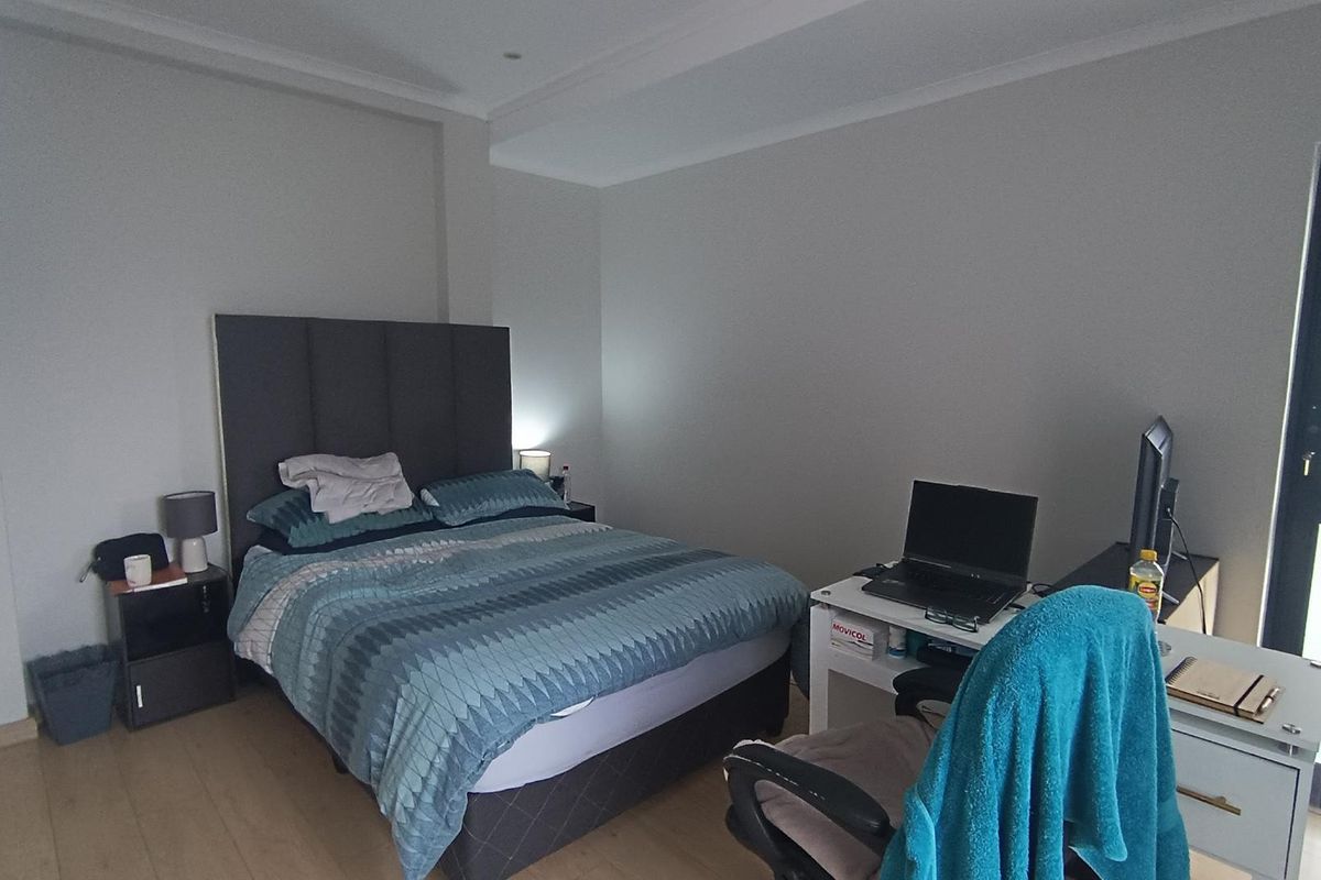 A well-maintained bedroom featuring light laminate flooring, neutral wall tones, recessed ceiling lighting, and a glass panel door providing natural light.