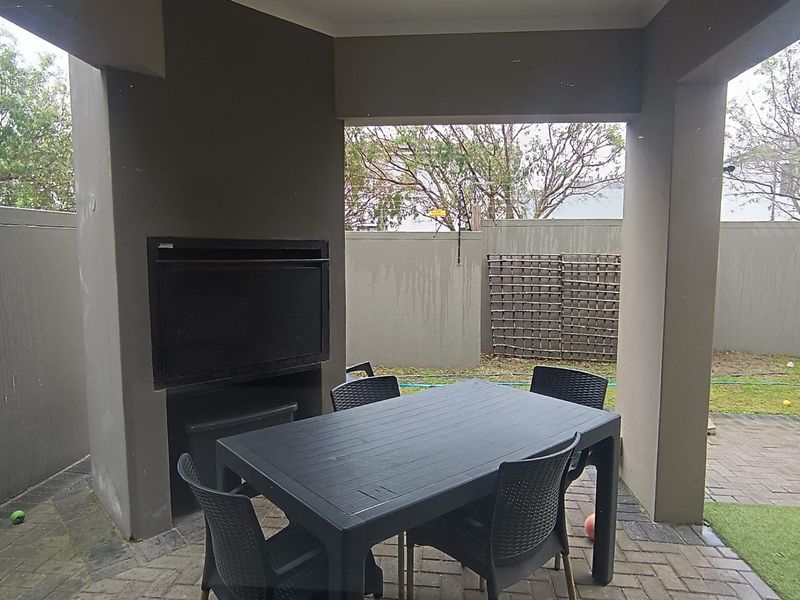 A covered patio area featuring a built-in braai and paved flooring, overlooking a private rear garden with boundary walls.