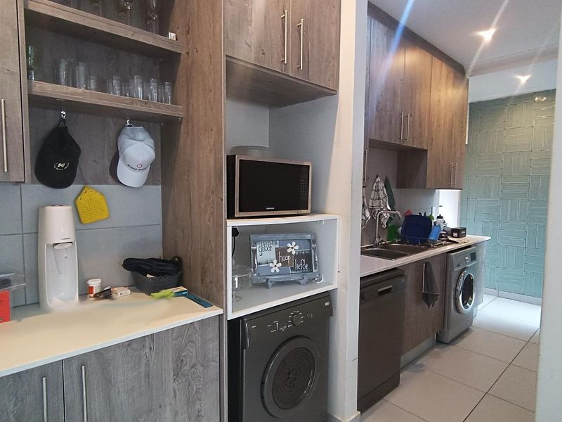 A functional scullery area featuring modern wood-look cabinetry, integrated appliance spaces, stainless steel sink, and tiled flooring.