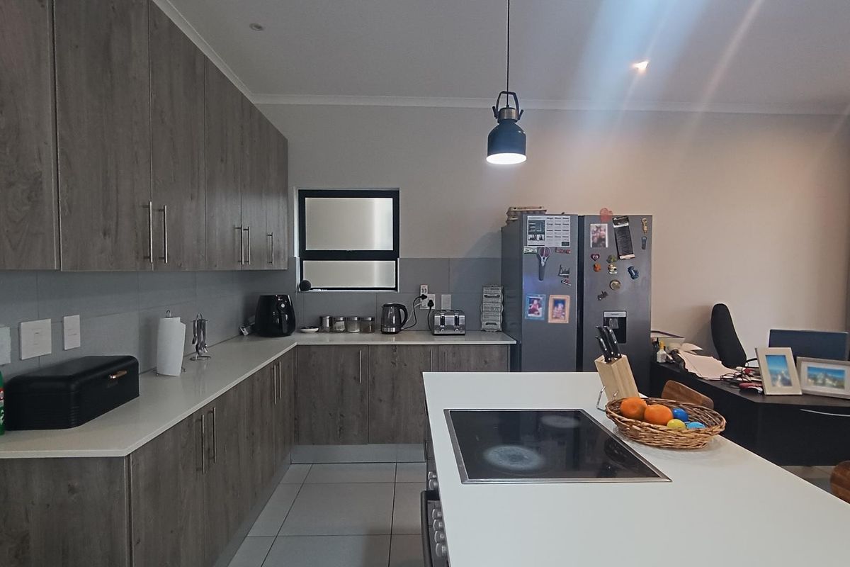 Modern kitchen featuring wood-grain cabinetry, stone countertops, a central island with an integrated electric hob, and tiled flooring.