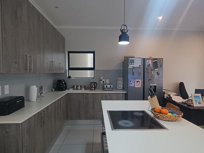 Modern kitchen featuring wood-grain cabinetry, stone countertops, a central island with an integrated electric hob, and tiled flooring.