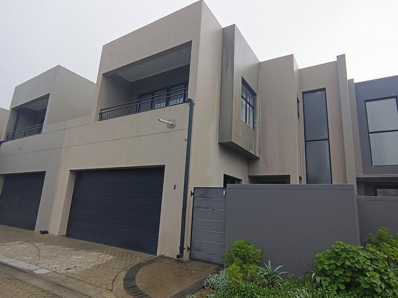 Modern double-storey townhouse featuring a double garage, upper-level balcony, and contemporary facade with paved driveway access.