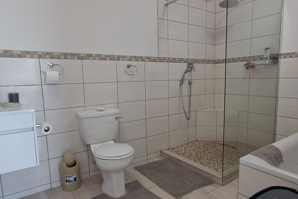 A functional bathroom featuring a vanity, toilet, glass-enclosed shower, and a bathtub with neutral wall and floor tiling.