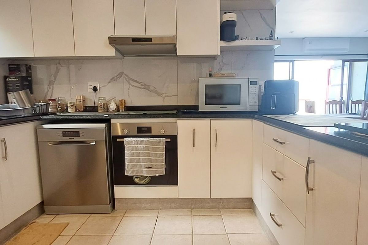 A functional kitchen featuring white cabinetry, granite countertops, a stainless steel oven, extractor fan, and integrated dishwasher with tiled flooring and backsplash.