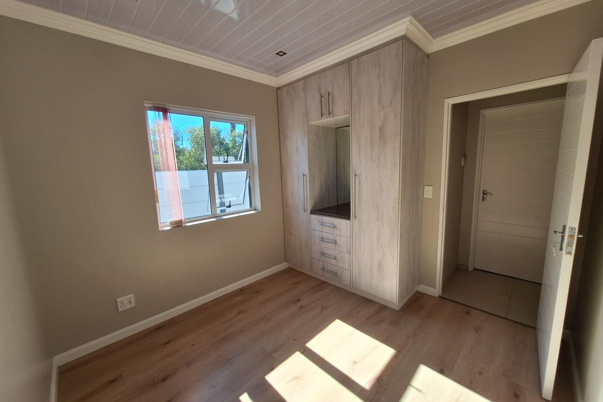 A bright, empty bedroom featuring modern laminate flooring, built-in cupboards with integrated vanity, and a clean, neutral aesthetic.