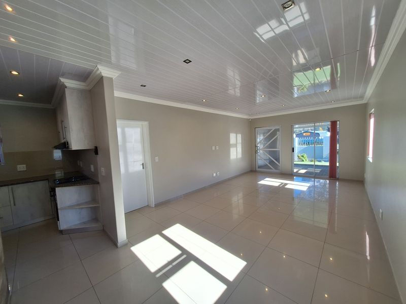 Spacious open-plan living area featuring glossy tiled floors, modern PVC ceiling panels, recessed lighting, and an integrated kitchen with built-in cabinetry.