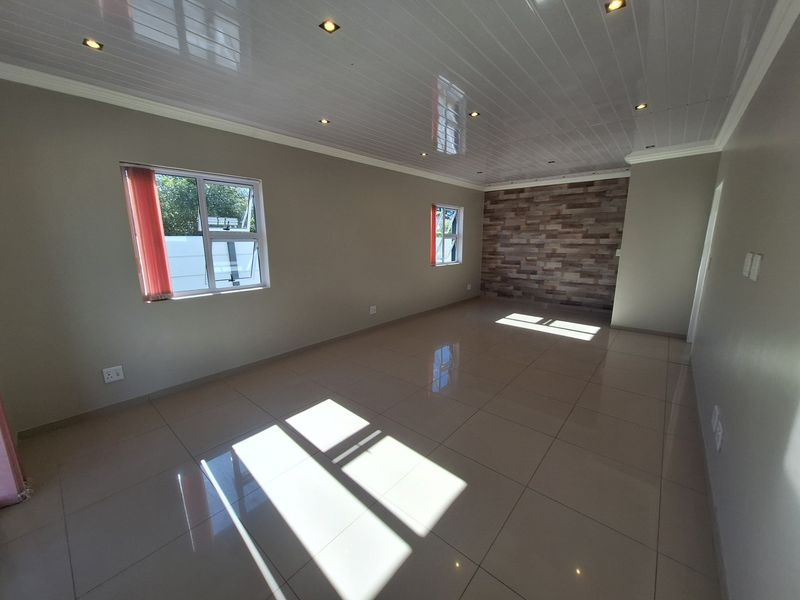 A spacious, empty living area featuring polished floor tiles, a modern feature wall, and recessed downlighting throughout the room.
