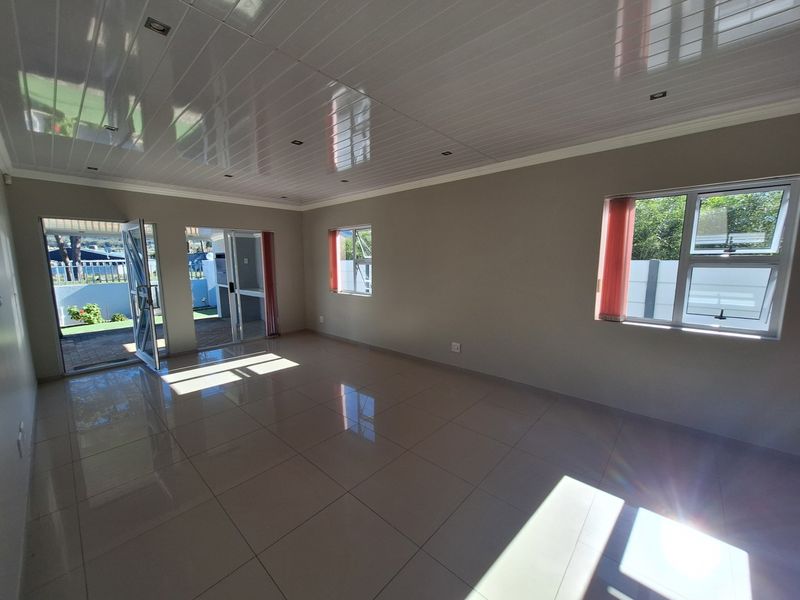 A bright, spacious, and empty living area featuring polished floor tiles, modern PVC ceiling panels, and large aluminium sliding doors leading to the exterior.