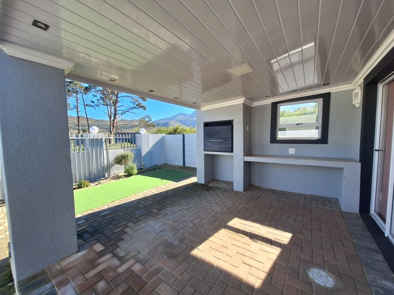 A covered patio area featuring a built-in braai, concrete prep counter, recessed lighting, and paved flooring, overlooking a small garden with mountain views.