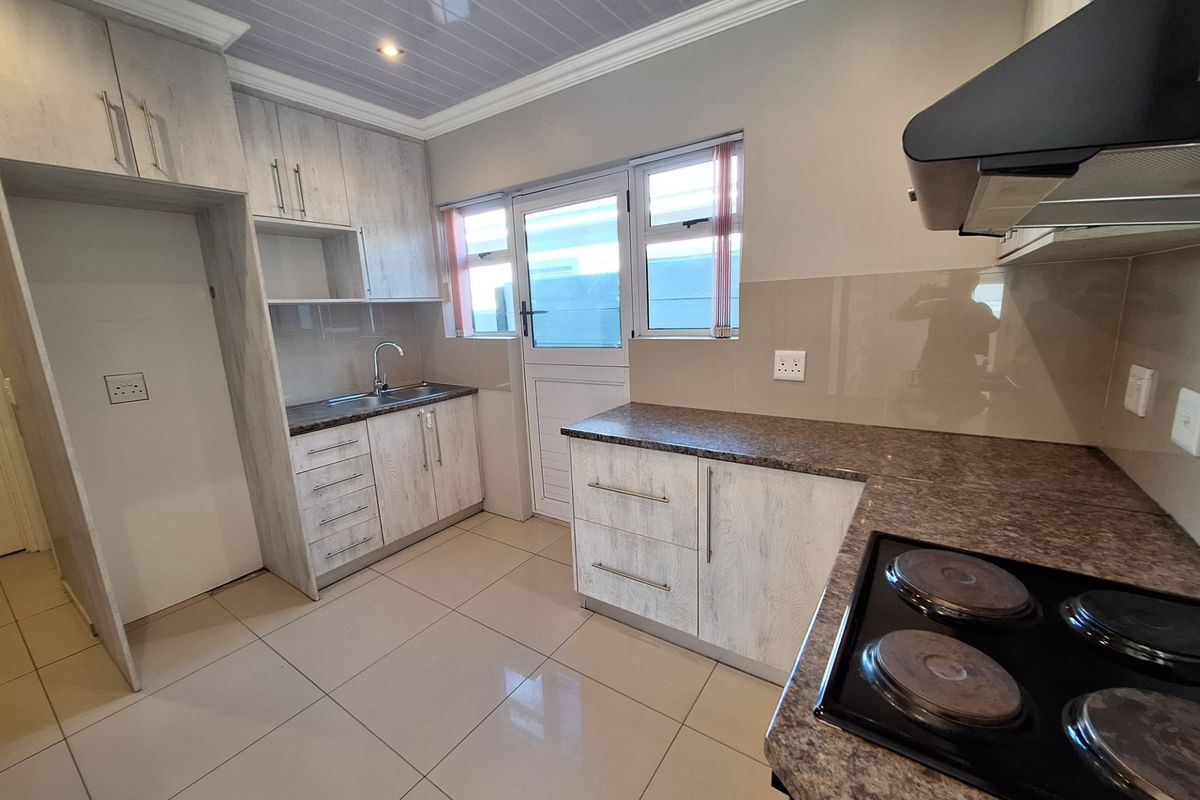 A clean, functional kitchen featuring light wood-grain cabinetry, granite-look countertops, an electric hob with extractor, and tiled flooring with direct exterior access.