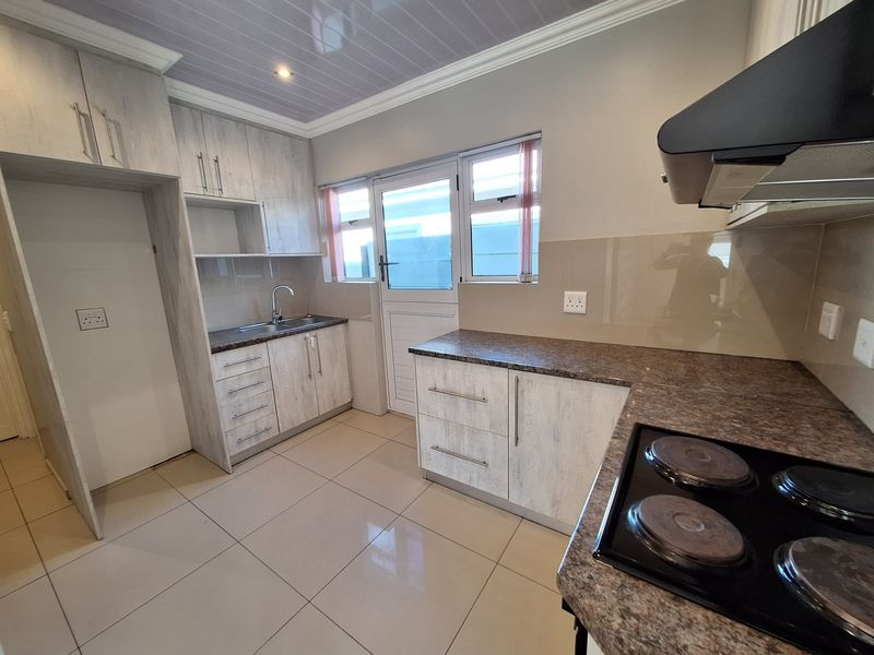 A clean, functional kitchen featuring light wood-grain cabinetry, granite-look countertops, an electric hob with extractor, and tiled flooring with direct exterior access.