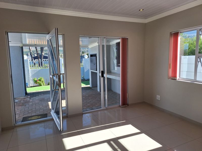 Bright, empty living area featuring tiled floors, recessed lighting, and direct access to a covered patio with a built-in braai.
