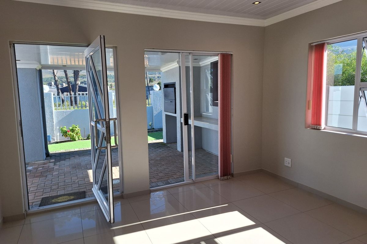 Bright, empty living area featuring tiled floors, recessed lighting, and direct access to a covered patio with a built-in braai.