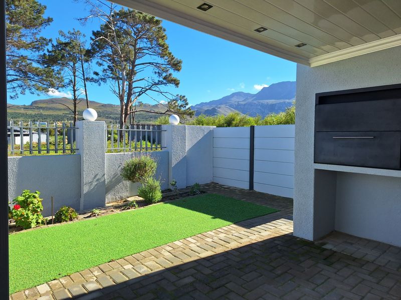 A covered patio area featuring a built-in braai, paved flooring, and artificial turf, offering scenic mountain views.