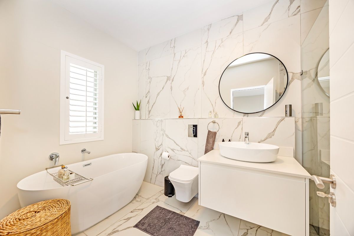 Modern bathroom featuring a freestanding bathtub, wall-mounted toilet, floating vanity with vessel sink, and elegant marble-look wall tiling.