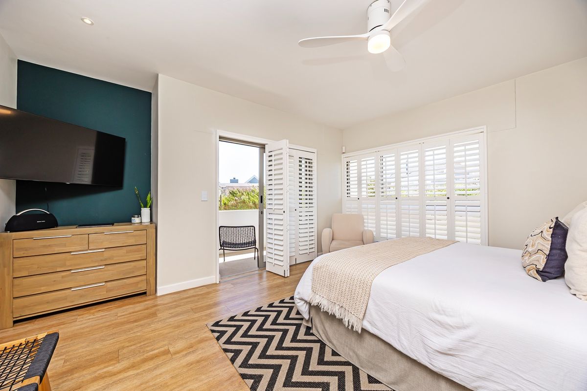 A well-maintained bedroom featuring laminate flooring, plantation shutters, a ceiling fan, and direct access to a private balcony.