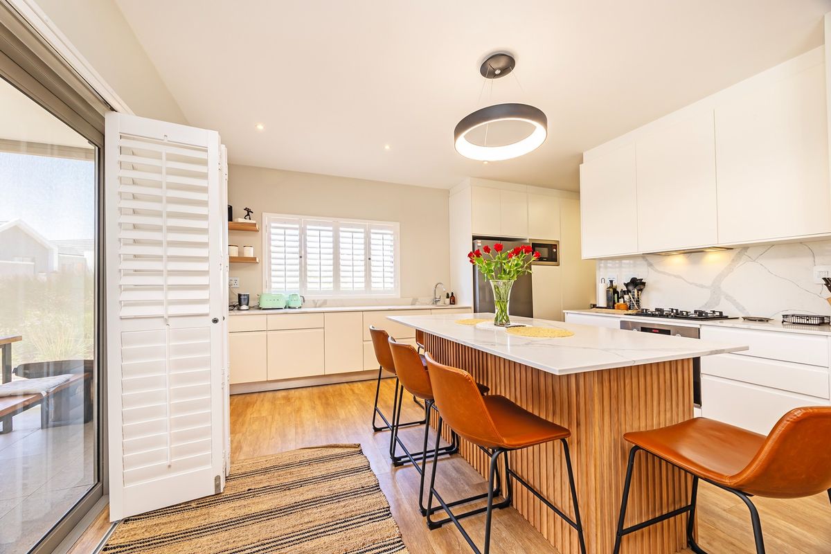 Modern kitchen featuring a central island with stone countertops, sleek cabinetry, built-in appliances, and direct access to an outdoor patio area.