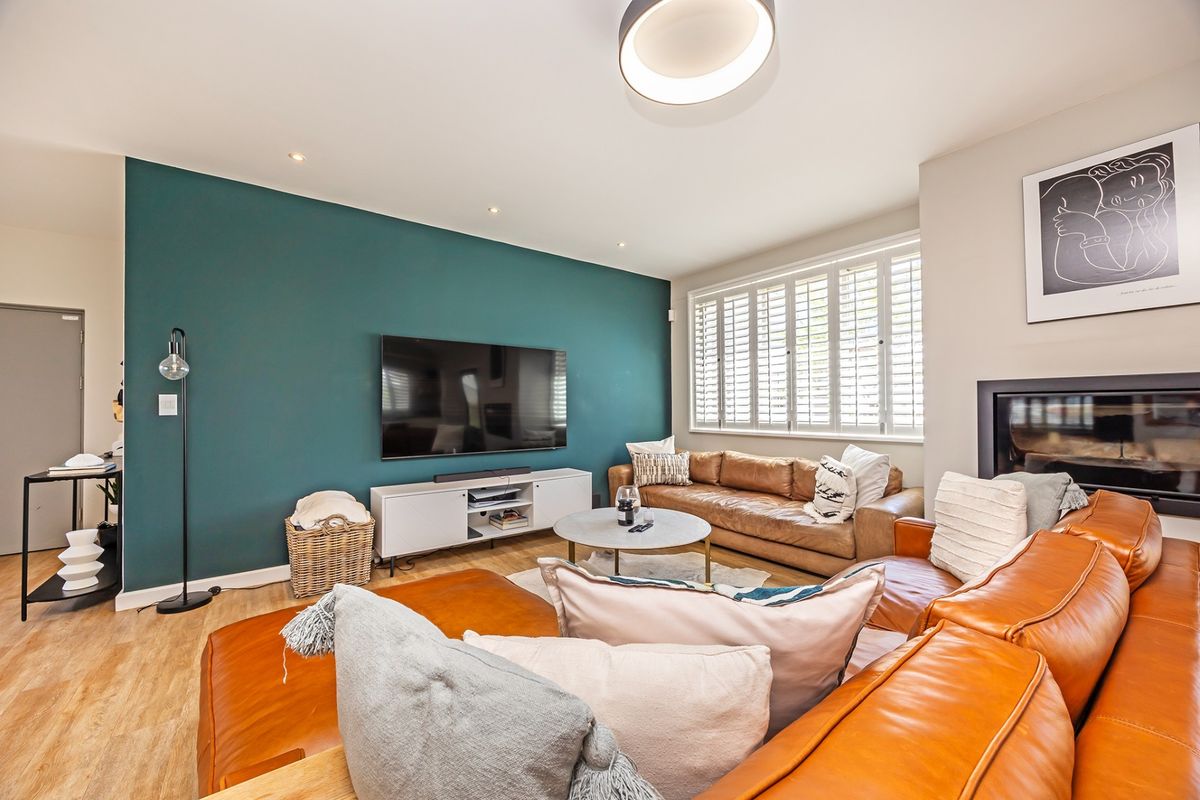 A well-presented living room featuring a bold teal accent wall, plantation shutters, recessed lighting, and a built-in fireplace.