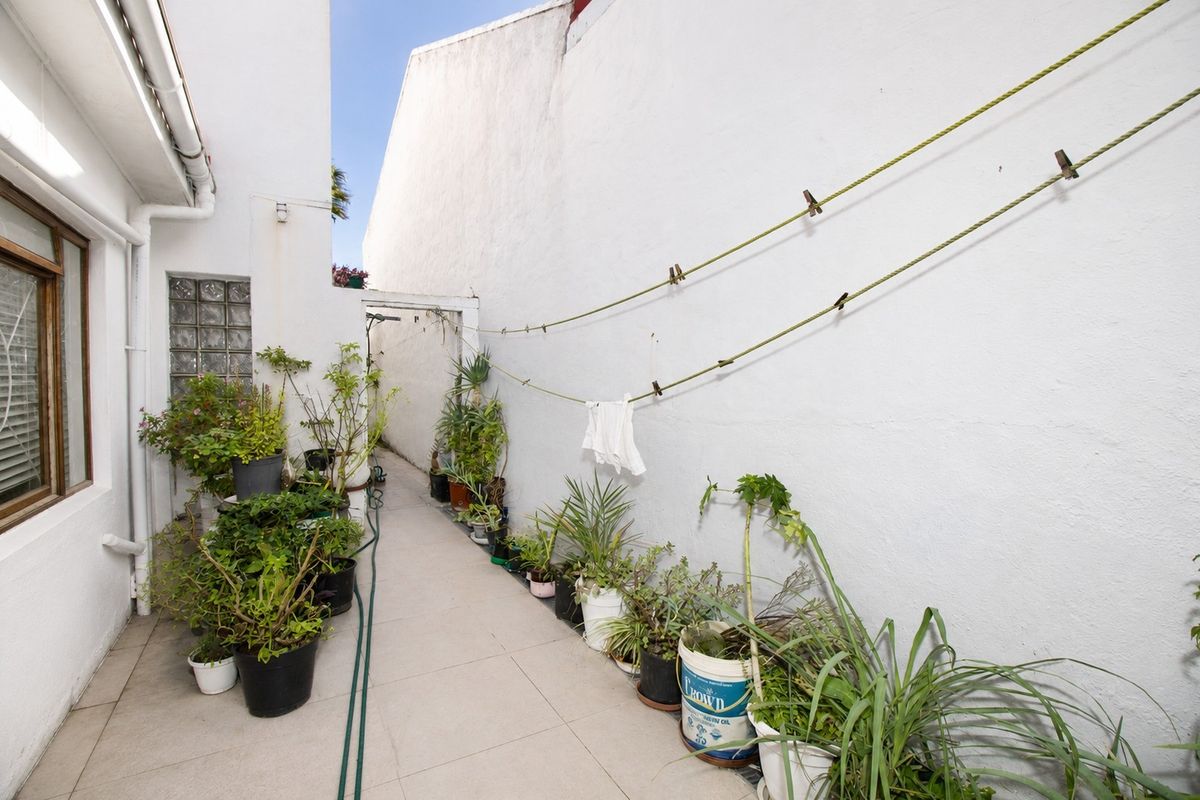 A narrow side courtyard or utility passage featuring tiled flooring, a glass block window, and a fixed washing line against a rendered wall.