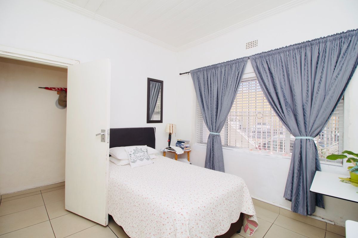 A functional bedroom featuring tiled flooring, security bars on the window, and a neutral interior finish.