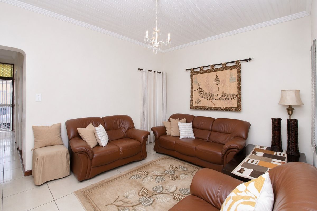 A comfortable living room featuring tiled flooring, a classic tongue and groove ceiling with cornice detailing, and an arched entryway.