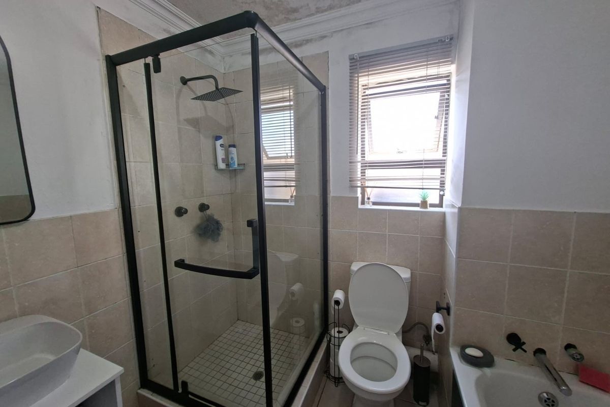 A compact bathroom featuring a glass shower enclosure, bathtub, and vessel sink, currently showing signs of ceiling water damage requiring maintenance.