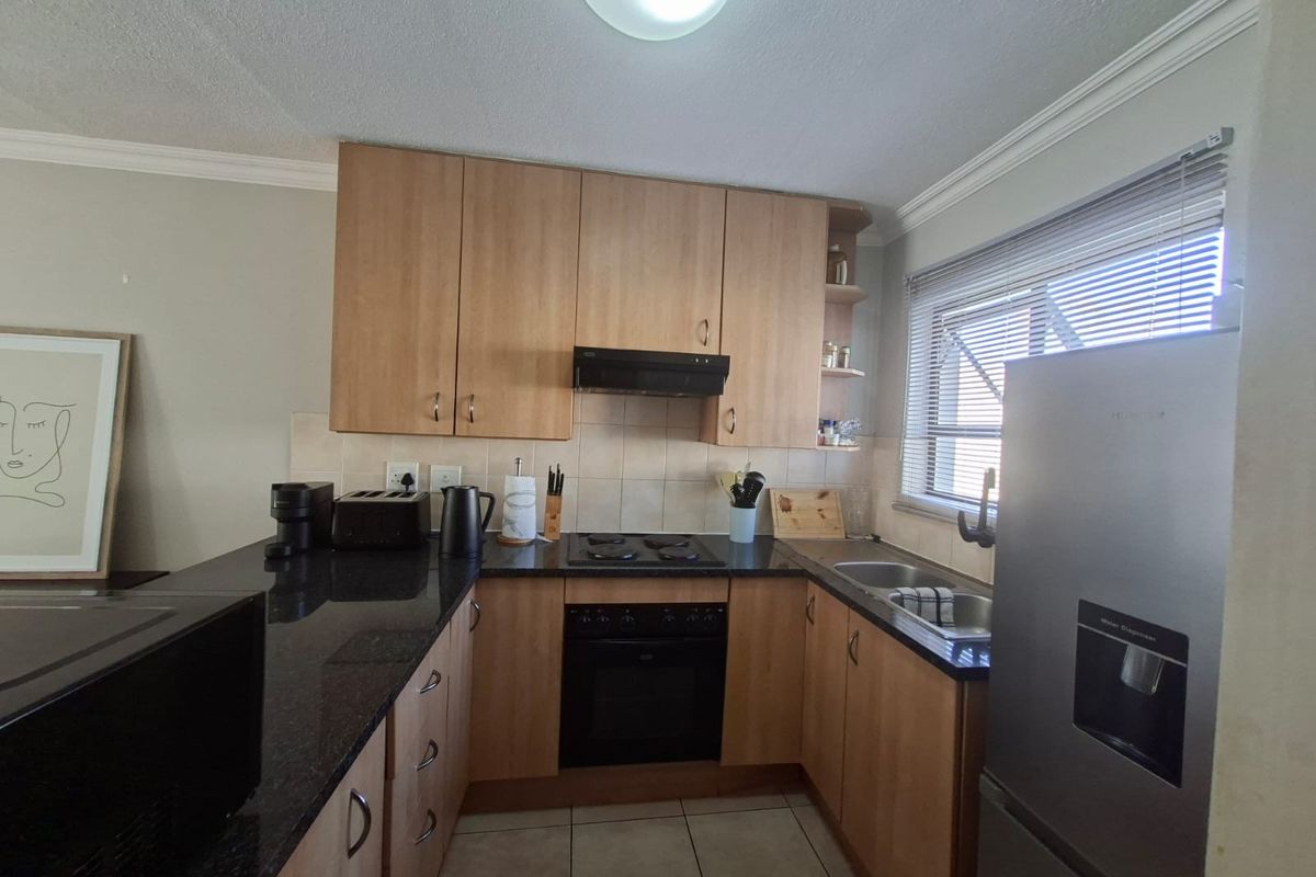 A functional kitchen featuring laminate cabinetry, granite countertops, a built-in oven with hob, extractor fan, and a double sink with tiled backsplash.