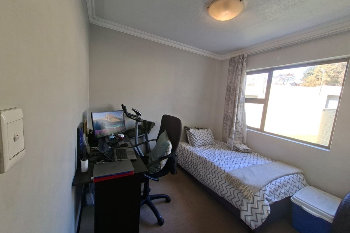 A functional bedroom featuring neutral walls, carpeted flooring, and a large window providing natural light, suitable for use as a guest room or home office.
