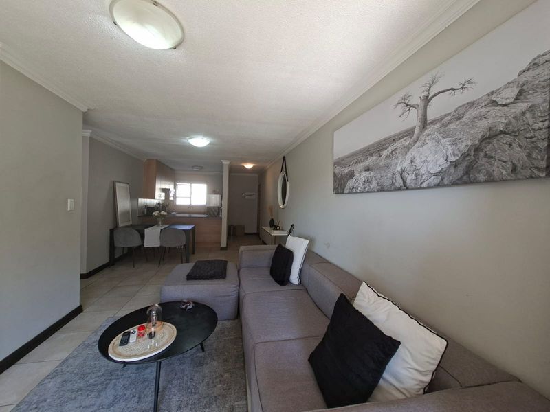 Open plan living and kitchen area featuring tiled flooring, neutral wall tones, and functional kitchen cabinetry in a well-maintained apartment setting.