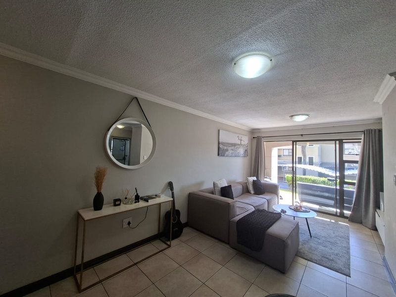 A comfortable living room featuring tiled flooring, coved ceilings, and a large sliding glass door providing access to an outdoor balcony area.