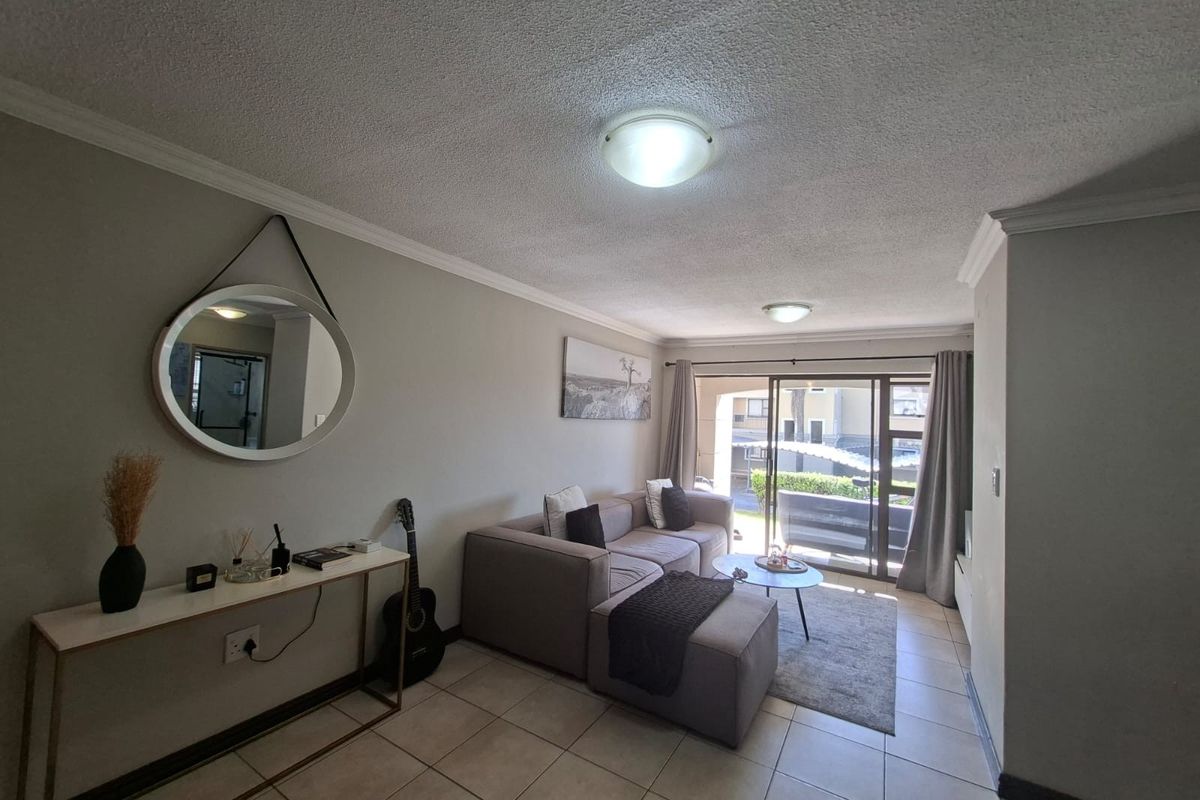 A well-lit living room featuring neutral tiled flooring, coved cornices, and a sliding glass door providing access to an outdoor patio area.
