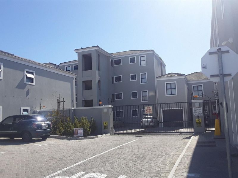 Exterior view of the apartment complex entrance featuring a secure gated access point, paved driveway, and perimeter security fencing.