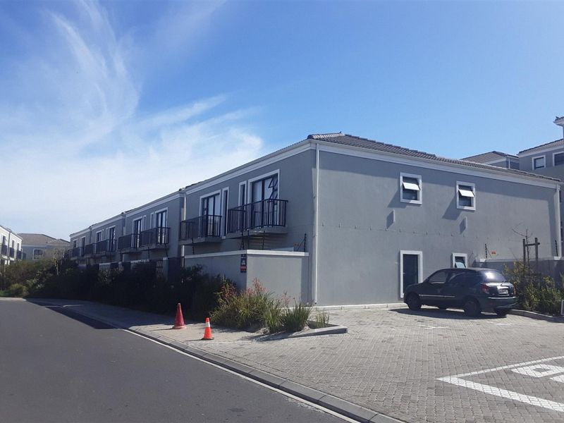 Exterior view of a modern apartment complex featuring paved parking, balconies, and secure perimeter fencing.